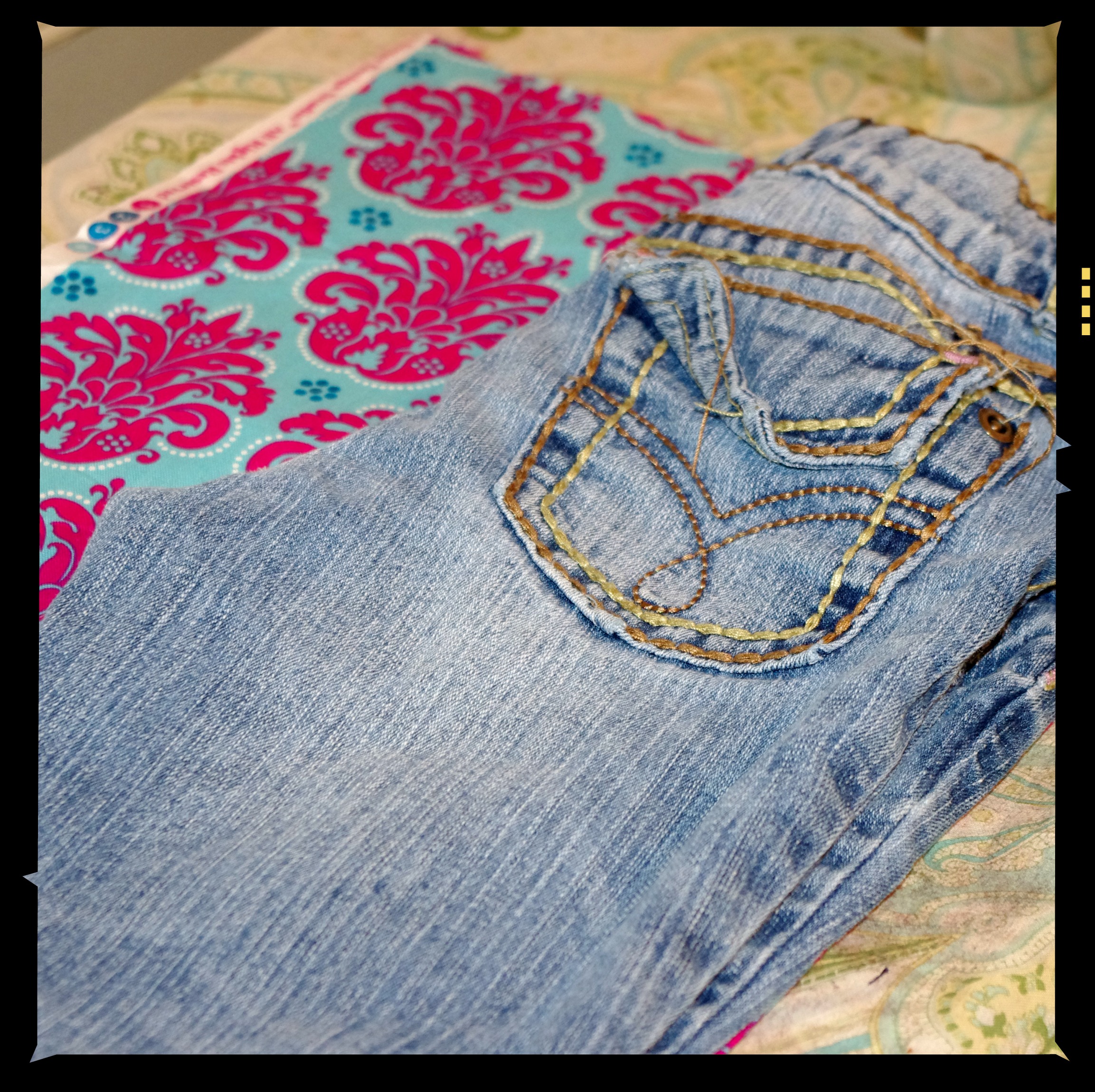 Jeans laid out on top of hot pink and blue damask fabric. 