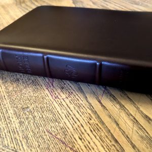Close up of spine of Heirloom Bible Alpha Edition on wood table with scribble marks on it. 